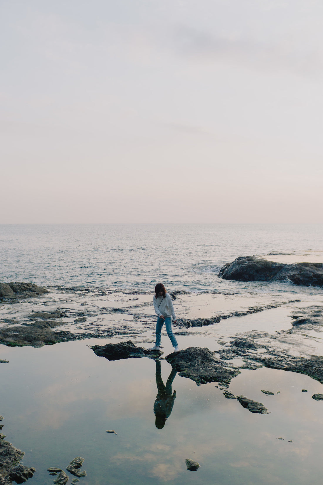 Frau am Meer, Felsen ragen aus dem Wasser, Sonnenuntergangsstimmung